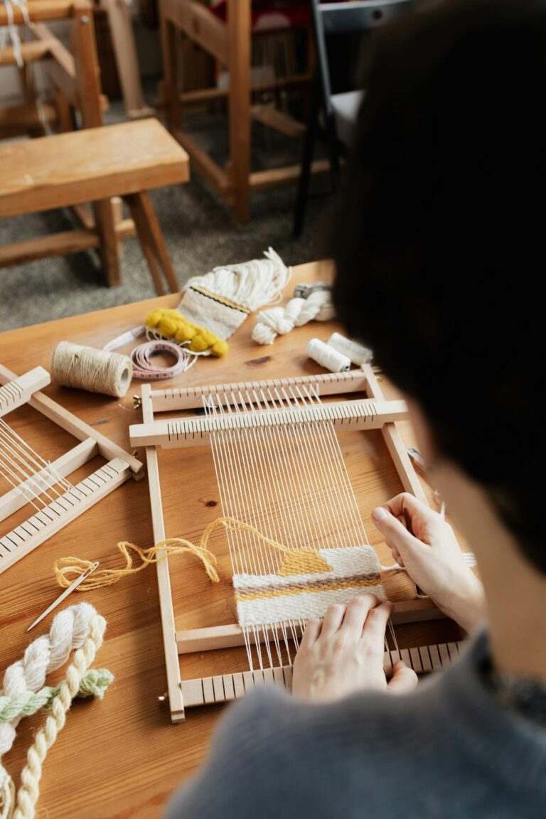 A craftsman skillfully weaves on a hand loom at a wooden table indoors.