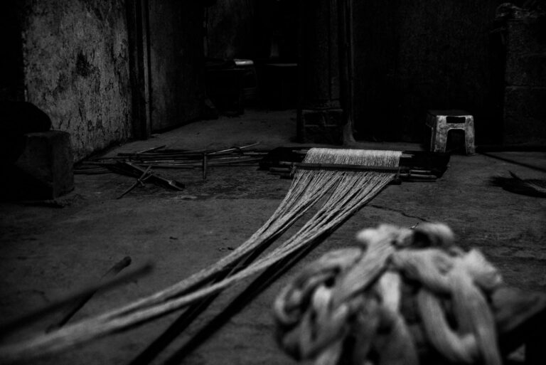 A dramatic black and white photo of industrial weaving equipment featuring ropes and strings.